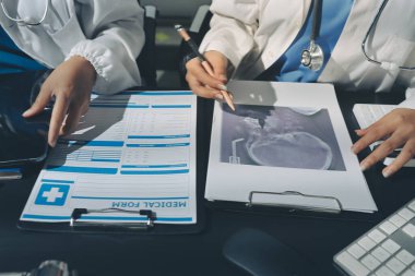 Two doctors and a female nurse meet at a table in the hospital, collaborating on medical tasks using laptops and computers