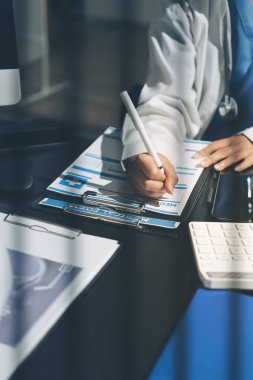 Two doctors and a female nurse meet at a table in the hospital, collaborating on medical tasks using laptops and computers