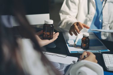 Two doctors and a female nurse meet at a table in the hospital, collaborating on medical tasks using laptops and computers