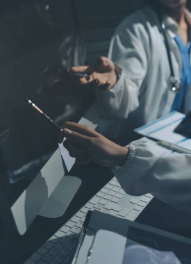 Two doctors and a female nurse meet at a table in the hospital, collaborating on medical tasks using laptops and computers
