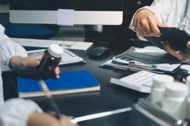 Two doctors and a female nurse meet at a table in the hospital, collaborating on medical tasks using laptops and computers