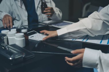 Two doctors and a female nurse meet at a table in the hospital, collaborating on medical tasks using laptops and computers