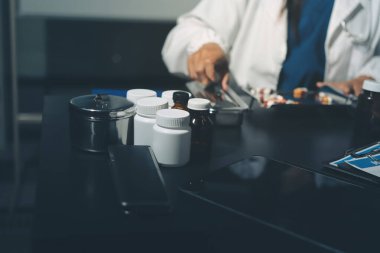 Two doctors and a female nurse meet at a table in the hospital, collaborating on medical tasks using laptops and computers