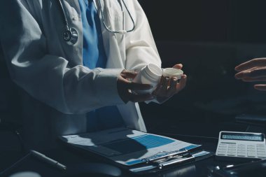 Two doctors and a female nurse meet at a table in the hospital, collaborating on medical tasks using laptops and computers