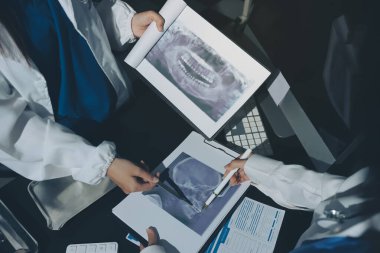 Two doctors and a female nurse meet at a table in the hospital, collaborating on medical tasks using laptops and computers