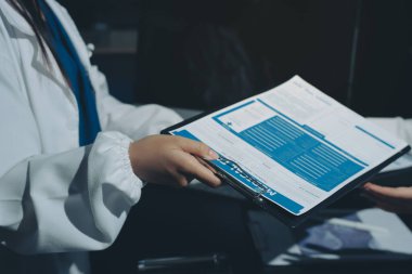 Two doctors and a female nurse meet at a table in the hospital, collaborating on medical tasks using laptops and computers