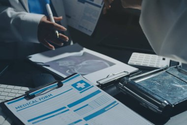 Two doctors and a female nurse meet at a table in the hospital, collaborating on medical tasks using laptops and computers