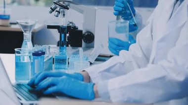 Yakın plan - test tüpü tutan ve dizüstü bilgisayarda çalışan bilim adamlarının elleri
