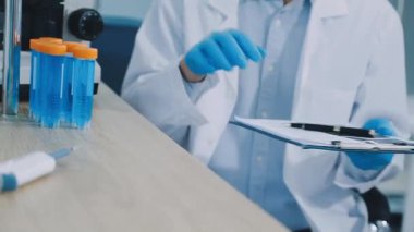 Laboratuvar asistanı deney tüpüyle matara tutuyor.