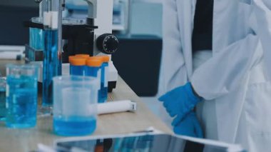 Bilim adamı bardağı sıvıyla, test tüpünü de sıvıyla tutuyor.