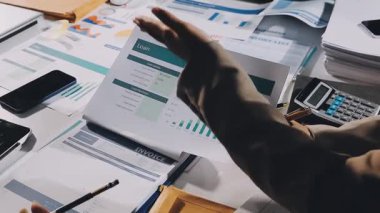 Genç iş adamı dizüstü bilgisayardaki finansal istatistikleri analiz ediyor. İş adamları finansal raporu tartışıyor ve modern işyerinde verileri analiz ediyorlar.