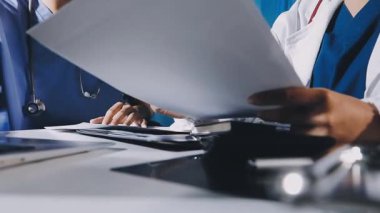 Doktorlar modern tıp bürosunda toplanıyor. Laptop, tablet ve tıbbi ekipmanlarla çalışıyorlar..