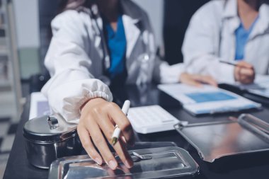 Two doctors and a female nurse meet at a table in the hospital, collaborating on medical tasks using laptops and computers