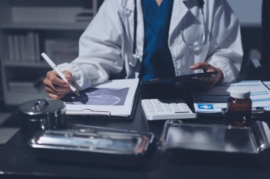 Two doctors and a female nurse meet at a table in the hospital, collaborating on medical tasks using laptops and computers