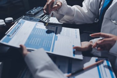 Two doctors and a female nurse meet at a table in the hospital, collaborating on medical tasks using laptops and computers