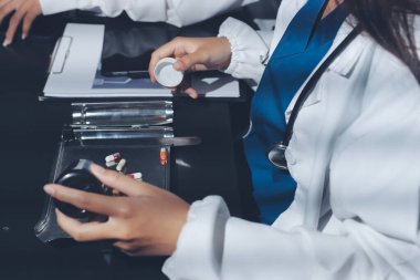 Two doctors and a female nurse meet at a table in the hospital, collaborating on medical tasks using laptops and computers