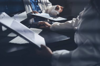 Two doctors and a female nurse meet at a table in the hospital, collaborating on medical tasks using laptops and computers