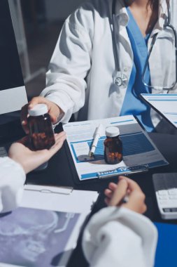 Two doctors and a female nurse meet at a table in the hospital, collaborating on medical tasks using laptops and computers