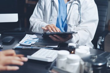 Two doctors and a female nurse meet at a table in the hospital, collaborating on medical tasks using laptops and computers