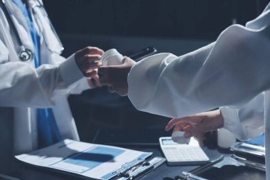 Two doctors and a female nurse meet at a table in the hospital, collaborating on medical tasks using laptops and computers