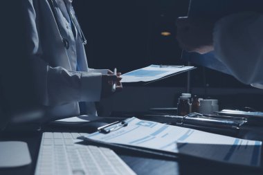 Two doctors and a female nurse meet at a table in the hospital, collaborating on medical tasks using laptops and computers