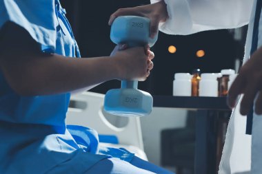 Fizyoterapist, halter egzersizinde bir kadına yardım ediyor.