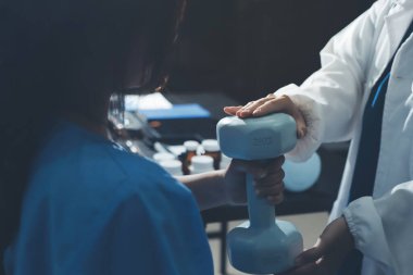 Fizyoterapist, halter egzersizinde bir kadına yardım ediyor.