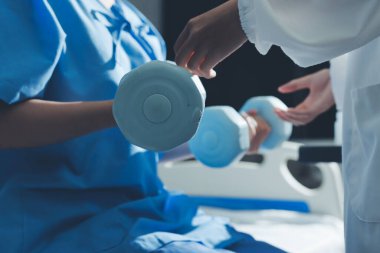 Fizyoterapist, halter egzersizinde bir kadına yardım ediyor.