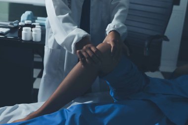 Hastane odasında yaralı bir kadının ayak bileğini inceleyen ve destekleyen doktor, burkulma ya da kırık için tıbbi yardım ve tedavi sunuyor.