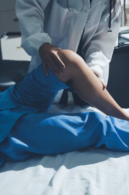 Hastane odasında yaralı bir kadının ayak bileğini inceleyen ve destekleyen doktor, burkulma ya da kırık için tıbbi yardım ve tedavi sunuyor.