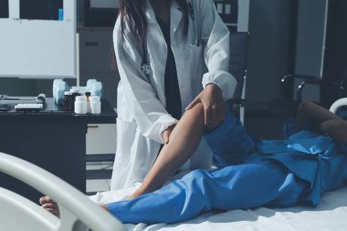 Hastane odasında yaralı bir kadının ayak bileğini inceleyen ve destekleyen doktor, burkulma ya da kırık için tıbbi yardım ve tedavi sunuyor.