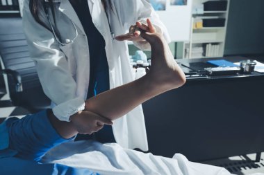 Hastane odasında yaralı bir kadının ayak bileğini inceleyen ve destekleyen doktor, burkulma ya da kırık için tıbbi yardım ve tedavi sunuyor.