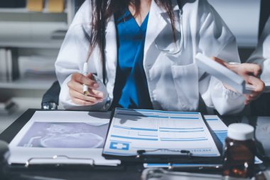 Two doctors and a female nurse meet at a table in the hospital, collaborating on medical tasks using laptops and computers