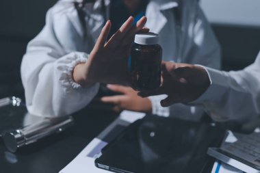 Two doctors and a female nurse meet at a table in the hospital, collaborating on medical tasks using laptops and computers