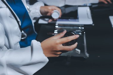 Two doctors and a female nurse meet at a table in the hospital, collaborating on medical tasks using laptops and computers