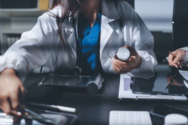 Two doctors and a female nurse meet at a table in the hospital, collaborating on medical tasks using laptops and computers