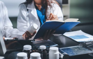 Two doctors and a female nurse meet at a table in the hospital, collaborating on medical tasks using laptops and computers