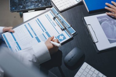 Two doctors and a female nurse meet at a table in the hospital, collaborating on medical tasks using laptops and computers