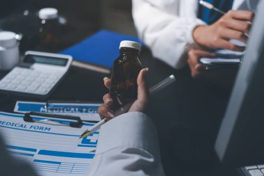 Two doctors and a female nurse meet at a table in the hospital, collaborating on medical tasks using laptops and computers
