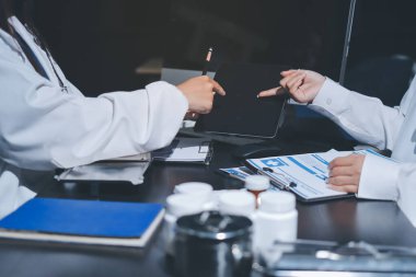 Two doctors and a female nurse meet at a table in the hospital, collaborating on medical tasks using laptops and computers