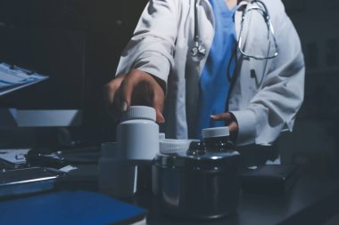 Two doctors and a female nurse meet at a table in the hospital, collaborating on medical tasks using laptops and computers