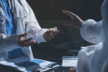 Two doctors and a female nurse meet at a table in the hospital, collaborating on medical tasks using laptops and computers