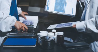 Two doctors and a female nurse meet at a table in the hospital, collaborating on medical tasks using laptops and computers