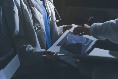 Two doctors and a female nurse meet at a table in the hospital, collaborating on medical tasks using laptops and computers