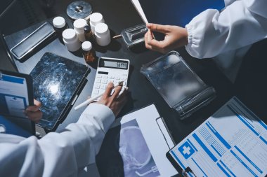 Two doctors and a female nurse meet at a table in the hospital, collaborating on medical tasks using laptops and computers