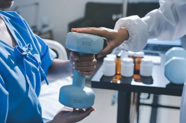 Fizyoterapist, halter egzersizinde bir kadına yardım ediyor.