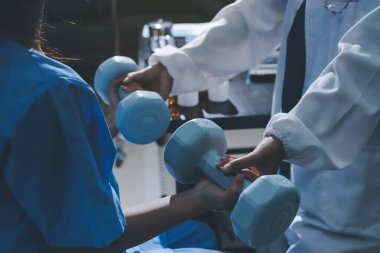 Fizyoterapist, halter egzersizinde bir kadına yardım ediyor.