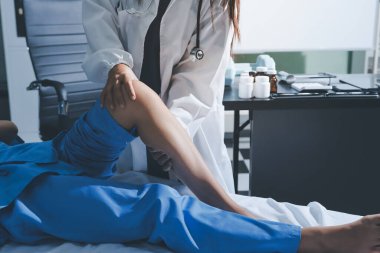 Hastane odasında yaralı bir kadının ayak bileğini inceleyen ve destekleyen doktor, burkulma ya da kırık için tıbbi yardım ve tedavi sunuyor.