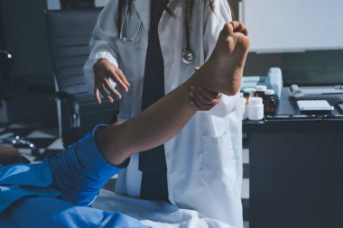 Hastane odasında yaralı bir kadının ayak bileğini inceleyen ve destekleyen doktor, burkulma ya da kırık için tıbbi yardım ve tedavi sunuyor.