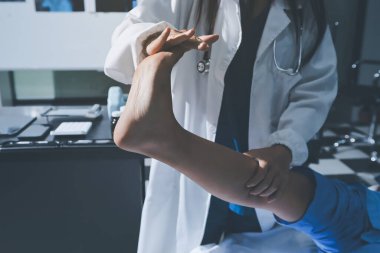 Hastane odasında yaralı bir kadının ayak bileğini inceleyen ve destekleyen doktor, burkulma ya da kırık için tıbbi yardım ve tedavi sunuyor.